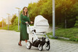 a woman in a green dress walks with a stroller. A young mother walks with a white color stroller on a sunny day.