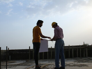 Two engineers standing at construction site looking at blueprints