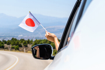 Wall Mural - Woman holding Japan flag from the open car window driving along the serpentine road in the mountains. Concept