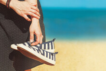 Female Hands  Holding Summer Shoes On The Seaside Background. Concept Of Summer Vacation.