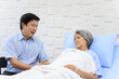 © DG PhotoStock - Senior Asian female patient resting on the medical bed in hospital and talking to her son.