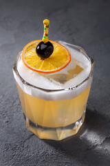 A cocktail with ice, froth, olive on a skewer and an orange