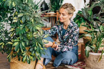 Wall Mural - A young woman takes care of potted plants while sitting on the floor in a workshop.