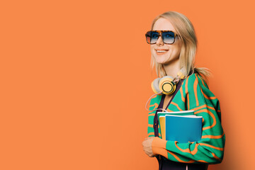 Poster - Stylish 80s woman in eyeglasses and headphones with notebooks on orange background