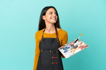 Wall Mural - Young artist caucasian woman holding a palette isolated on blue background thinking an idea while looking up