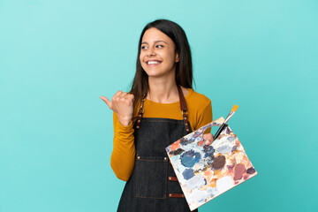 Wall Mural - Young artist caucasian woman holding a palette isolated on blue background pointing to the side to present a product