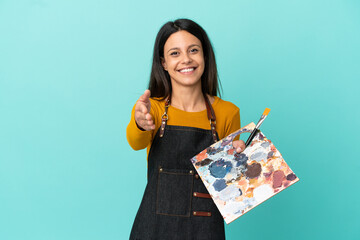 Wall Mural - Young artist caucasian woman holding a palette isolated on blue background shaking hands for closing a good deal