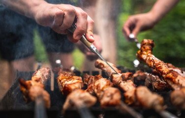 People trying barbecue delicious grilled meat with knife. Beautiful view on preparing pork steaks on fired charcoals with smoke. Hot BBQ closeup