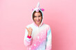 © luismolinero - Young caucasian woman with unicorn pajamas isolated on pink background pointing to the side to present a product