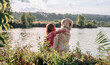 Child girl sitting and hugging golden retriever dog outdoors at the nature and looking at the lake. Teen kid with doggy pet resting close to river