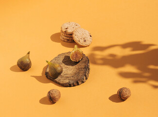 Wall Mural - Vintage style composition made of figs on wooden podium, cookies and nuts on orange background. Retro style food concept.