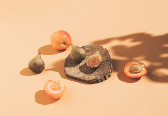 Wall Mural - Vintage style composition made of figs on wooden podium, apricots and tree shadow on orange background. Retro style food concept.