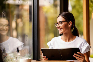 A happy girl is sitting in a bar and choosing a drink from a menu. 