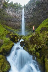 Wall Mural - A woman standing on the rock at Beautiful falls in forest, West coast USA. Watson Falls is waterfall on Watson Creek, a tributary of the Clearwater River, in Douglas County in the U.S. state 