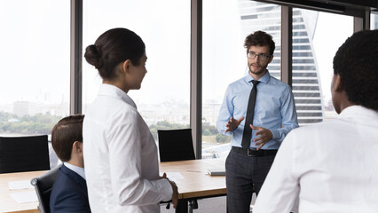 Wall Mural - Serious male boss and diverse employees talking, discussing work issues in office. Multiethnic workers listening to speaking business leader, executive, CEO at meeting in office