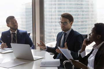 Wall Mural - Confident Caucasian businessman, team leader speaking at corporate meeting. Diverse colleagues, business partners, discussing project, brainstorming, negotiating on deal in office