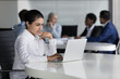 © fizkes - Focused busy young Indian worker woman using computer in co-working space, working at workplace table, typing, reading text, watching online project content. Business team meeting in background