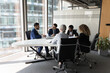 © fizkes - Millennial diverse different aged business team meeting in modern office space. Partners, stakeholders, colleagues negotiating at conference table at panoramic glass wall window