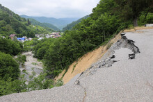 A Section Of Collapsed Asphalt. A Fragment Of The Highway Fell Into The Abyss. A Landslide That Damaged The Roadbed. Beautiful Green Mountains On The Background.