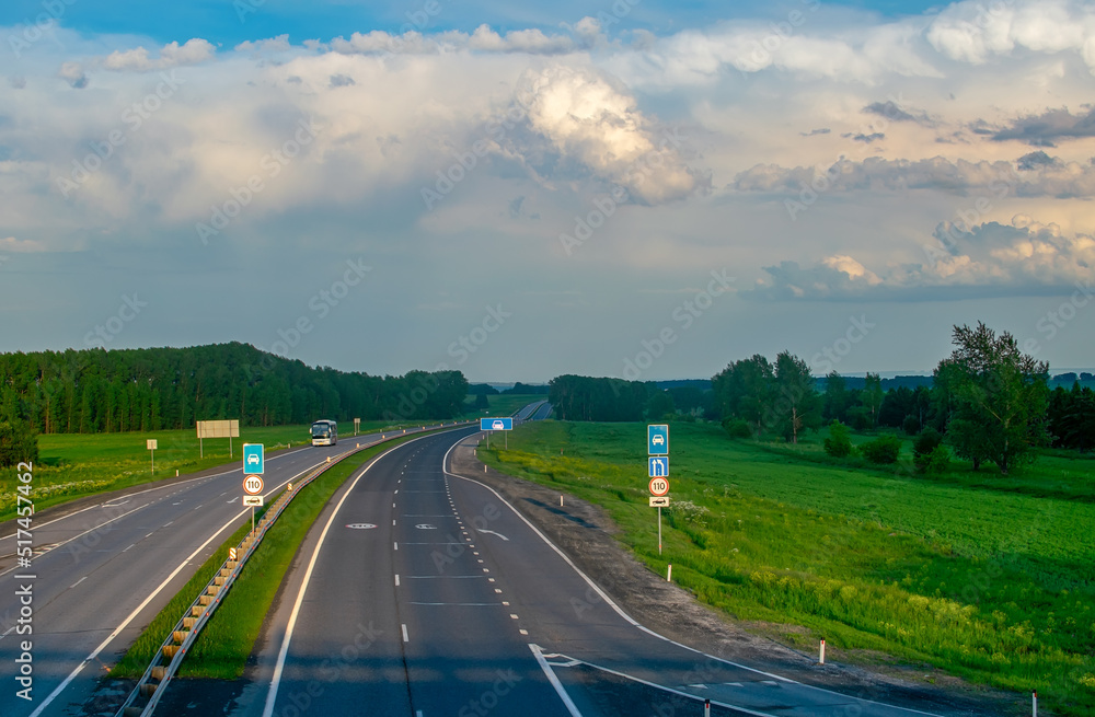 view of a summer paved highway with road signs among hills and a green ...