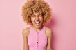 © WHstudio Leushin N - Portrait of cheerful curly haired woman exclaims loudly keeps mouth opened dressed in t shirt being very emotional reacts to something isolated over pink background. People and emotions concept
