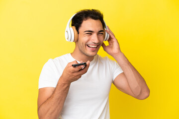 Wall Mural - Caucasian handsome man over isolated yellow background listening music with a mobile and singing