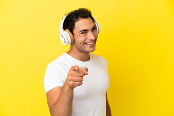 Wall Mural - Caucasian handsome man over isolated yellow background listening music and pointing to the front