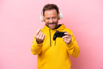 Wall Mural - Middle age man playing with a video game controller isolated on pink background making money gesture