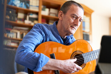 Wall Mural - Senior man listening to online classical guitar lesson