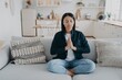 © VK Studio - Young mixed race woman is practicing yoga, sitting on couch in lotus pose with her eyes closed.