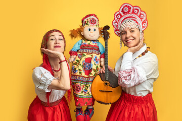 Wall Mural - Women musicians in Russian folk dresses with musical instruments on a yellow studio background. Happy artists from Russia in national clothes with stringed musical instruments with smiles on faces