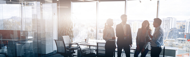 Wall Mural - Business team standing against panoramic windows in modern office. Blurred background