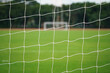 Blurred photo of football goal's net with background of firm grass pitch ground and the opposite site goal. Sport field equipment for background.