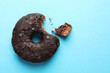 Sweet bitten glazed donut decorated with chocolate on light blue background, top view. Space for text