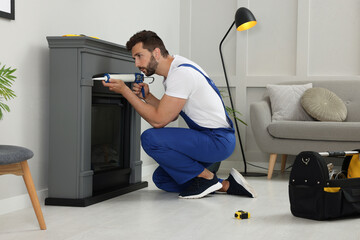 Canvas Print - Professional technician sealing electric fireplace with caulk near white wall in room