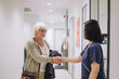 © Maskot - Smiling senior woman shaking hands with female doctor standing at doorway in hospital