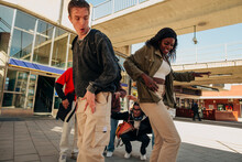 Multiracial Young Man And Woman Competing While Dancing On Street With Friends In Background