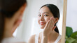 Leinwandbild Motiv Young Asian woman touching healthy facial skin look at mirror
