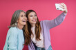 Leinwandbild Motiv Happy mother and adult daughter making selfie against pink background