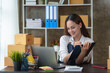 © amnaj - Happy young Asian business owner woman prepare parcel box and check online orders of product for deliver to customer on laptop computer. Shopping Online concept.