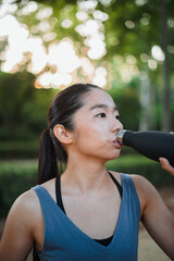 Close up shot of chinese teenager drinking water after jogging in the park