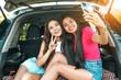 © Dmytro - Beautiful asian girls friends have fun and taking selfie on smartphone camera while sitting at the car trunk. Travel, happy lifestyle, good mood concept.