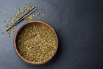 Bowl of gold nuggets and tweezers on black table, flat lay. Space for text