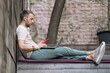 © DimaBerlin - Serious focused man young entrepreneur in glasses working on laptop online and using phone, sitting on wooden stairs outside, writing email. Male freelancer working remotely at outdoor environment