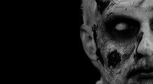 Close-up Face Of Sinister Man With Horrible Scary Halloween Zombie Makeup Making Faces, Looking Ominous At Camera, Trying To Scare. Dead Guy With Wounded Bloody Scars Face Isolated On Black Background