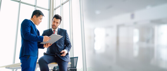 Two business people talk project strategy at office in widen view meeting room. Businessman discuss project planning with colleague at modern workplace .