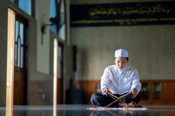 Wall Mural - A little Asian Muslim boy is sitting and reading the Quran. The peace in the mosque makes it an energetic atmosphere of faith, with copy space.