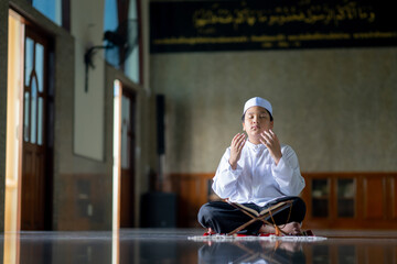 Wall Mural - A little Asian Muslim boy is praying with peace in the mosque, giving a powerful atmosphere of faith, with copy space.