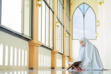 Portrait Asian Muslim woman reading the Quran and appreciates and faith The Holy Al Quran with written Arabic calligraphy meaning of Al Quran, Arabic word translation : The Holy Al Quran.