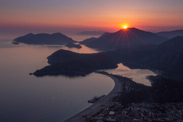 Fototapete - Unforgettable landscape of sunset above sea coast Oludeniz, Turkey. The sun sets behind the mountains, illuminating them with its rays. Beautiful red sky above town. View from lycian way.